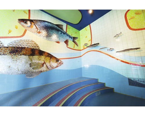 Wandgestaltung mit Mosaikfliesen in Fischoptik und geschwungener Treppe in einem Innenraum.