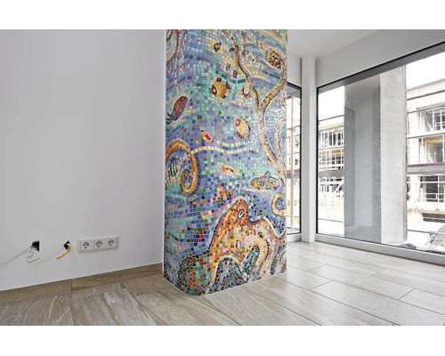 Eine runde Säule mit einem bunten Glasmosaik mit Unterwasser Motiven in einem modernen Raum mit Fliesenboden und großen Fensterfronten.