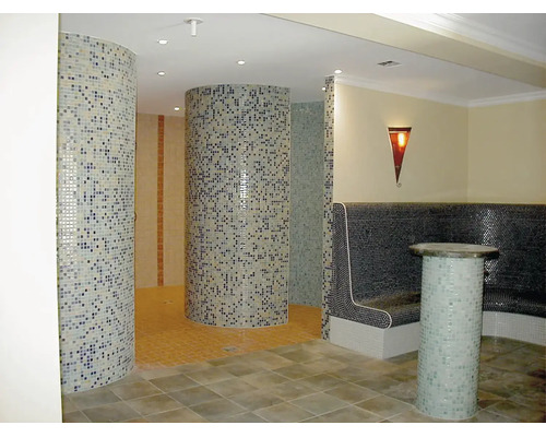 Wellnessbereich mit runden Duschkabinen aus Mosaikfliesen und Sitzbank mit Mosaikoberfläche sowie indirekter Beleuchtung.