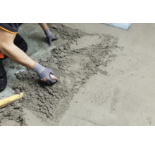 Handwerker beim Auftragen und Glattstreichen von Estrich oder Mörtel auf einem Boden mit einer Glättkelle.