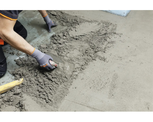 Handwerker beim Auftragen und Glattstreichen von Estrich oder Mörtel auf einem Boden mit einer Glättkelle.