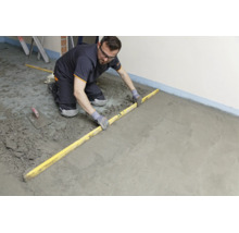 Handwerker glättet frischen Estrichboden mit einer Richtlatte auf einer Baustelle.