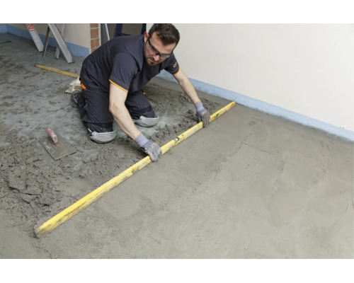 Handwerker glättet frischen Estrichboden mit einer Richtlatte auf einer Baustelle.