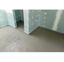 Baustelle mit frisch gegossenem Estrich auf dem Boden und Wänden aus Gipskartonplatten mit verspachtelten Fugen.