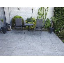 Gepflasterte Gartenterrasse mit Sitzgruppe aus zwei Klappstühlen und einem runden Bistrotisch, umgeben von Pflanzkübeln und Sträuchern.
