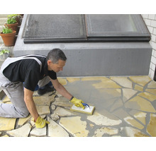 Handwerker beim Verfugen eines Bodenbelags aus Natursteinplatten mit einem Fugengummi auf einer Terrasse.