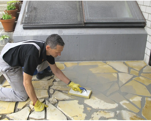 Handwerker beim Verfugen eines Bodenbelags aus Natursteinplatten mit einem Fugengummi auf einer Terrasse.