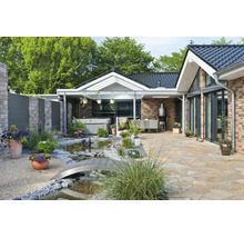 Gepflegte Terrasse mit Natursteinboden, kleinem Gartenteich mit Brücke, Whirlpool und überdachtem Sitzbereich vor einem modernen Backsteinhaus.