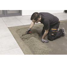 Handwerker beim Verlegen von Fliesen auf einem Drainagemörtelbett mit einer Glättkelle.