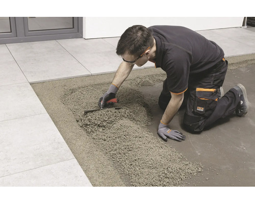 Handwerker beim Verlegen von Fliesen auf einem Drainagemörtelbett mit einer Glättkelle.