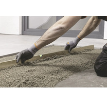 Handwerker beim Abziehen von Splittbett mit einer Richtlatte zur Vorbereitung für die Verlegung von Bodenplatten.