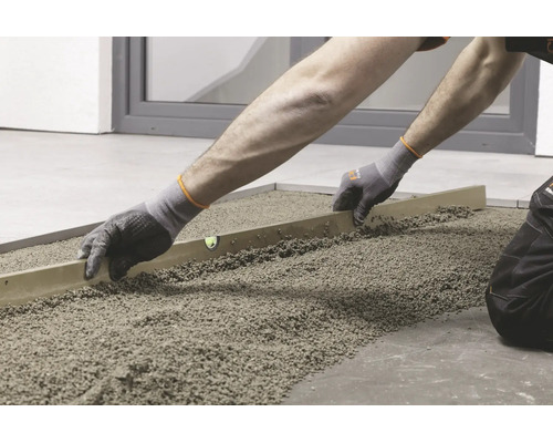 Handwerker beim Abziehen von Splittbett mit einer Richtlatte zur Vorbereitung für die Verlegung von Bodenplatten.