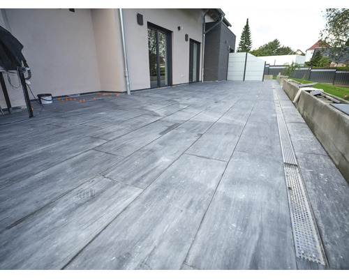 Terrasse mit großformatigen Fliesen in Steinoptik und integrierter Entwässerungsrinne vor einer modernen Hausfassade