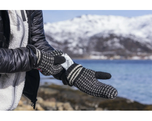 Eine Person mit Strickfäustlingen legt ein Thermopad Handwärmer in den Handschuh vor einer winterlichen Landschaft mit Berg und See.