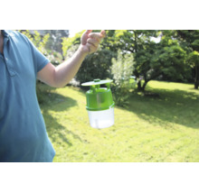 Eine Person hält eine Insektenfalle für den Außenbereich in die Höhe vor einem Garten.