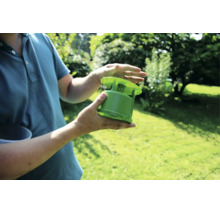 Eine Person hält eine grüne Insektenfalle in den Händen vor einem Gartenhintergrund.