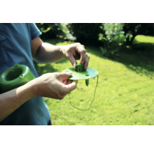 Person montiert Bewässerungshilfe mit Kunststoffdeckel und Schnur zur Pflanzenpflege im Garten.