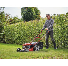 Ein Mann mäht Rasen mit einem benzinbetriebenen Rasenmäher von Einhell vor einer Hecke.