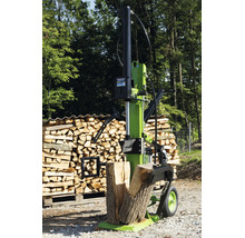 Ein vertikaler Holzspalter steht vor einem Holzstapel auf einem Waldweg.