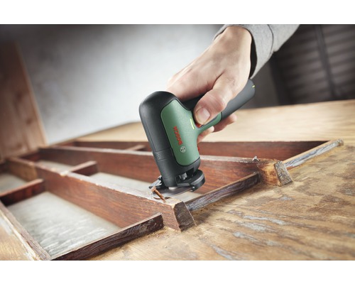 Eine Person benutzt ein Multifunktionswerkzeug von Bosch zum Bearbeiten eines Holzrahmens.