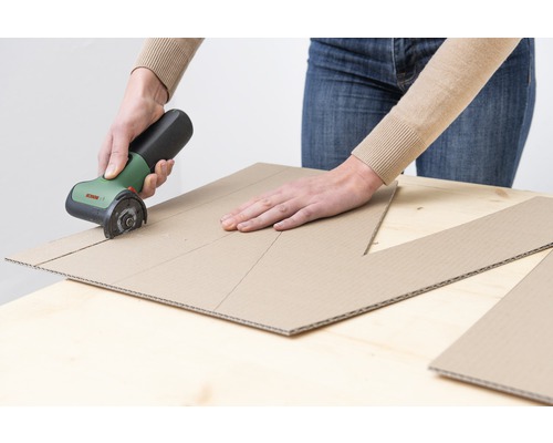 Person schneidet Pappe mit einem Elektromesser.