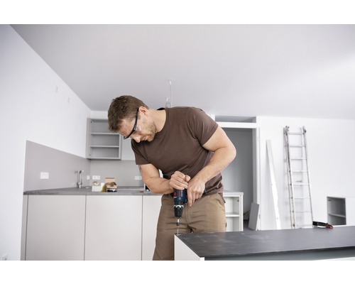 Mann mit Schutzbrille arbeitet mit Akku-Bohrschrauber in Küche