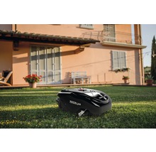 Schwarzer Rasenmähroboter der Marke Tech L20 auf einer Rasenfläche vor einem Wohnhaus.
