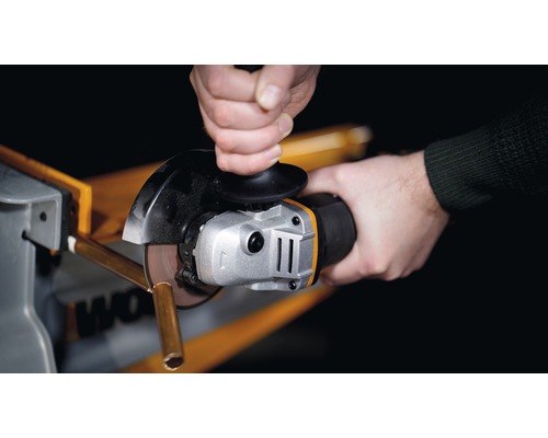 Nahaufnahme einer Person, die mit einem Winkelschleifer ein Metallrohr schneidet.