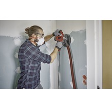 Ein Mann schleift eine Wand mit einem Trockenbauschleifer in einem Raum.