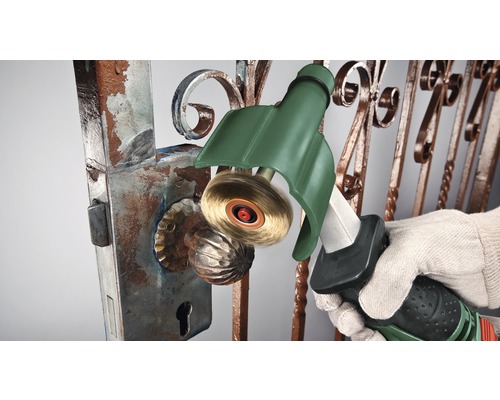 Eine Person entfernt Rost von einem Tor mit einer Drahtbürste.