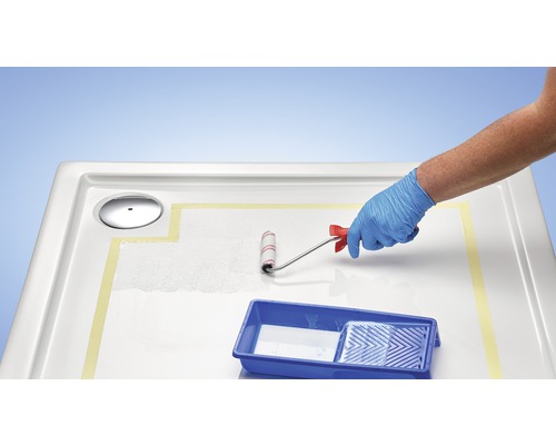 Eine Person trägt einen Schutzhandschuh und streicht eine Duschwanne mit einer Farbwalze.