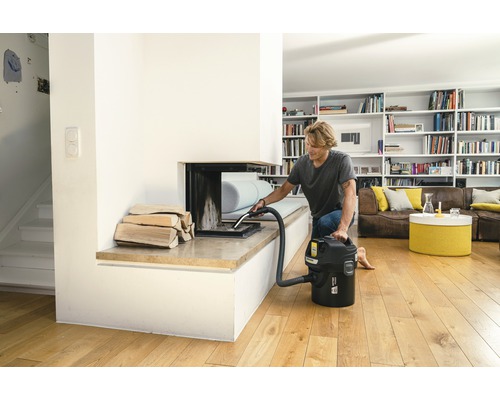 Mann reinigt Kamin mit Aschesauger in hellem Wohnzimmer