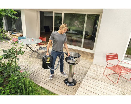 Ein Mann reinigt mit einem Aschesauger einen Grill auf einer Holzterrasse.