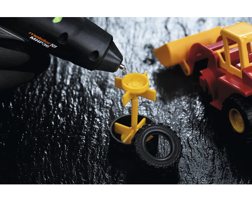 Heißklebepistole beim Kleben eines gelben Spielzeugteils an einem Spielzeugauto.