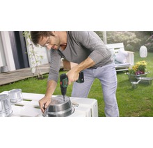 Ein Mann bohrt mit einem Akkuschrauber ein Loch in einen Metalltopf im Garten.
