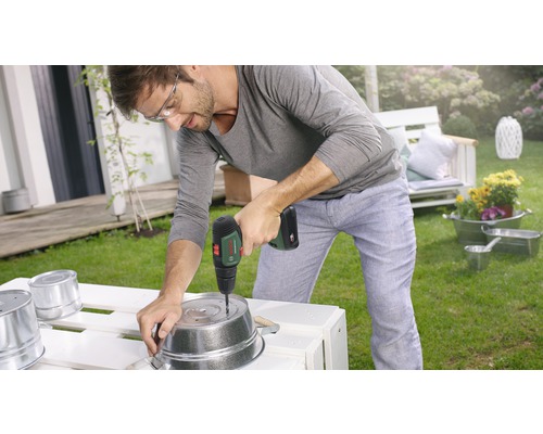 Ein Mann bohrt mit einem Akkuschrauber ein Loch in einen Metalltopf im Garten.