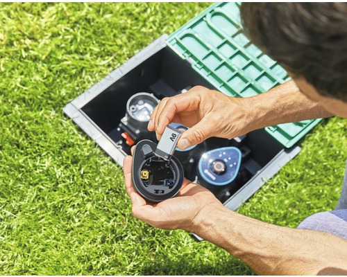 Mann legt Batterie in Bewässerungscomputer in einem Schacht im Rasen