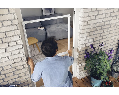 Mann montiert Insektenschutzgitter an Türrahmen in heller Wohnung