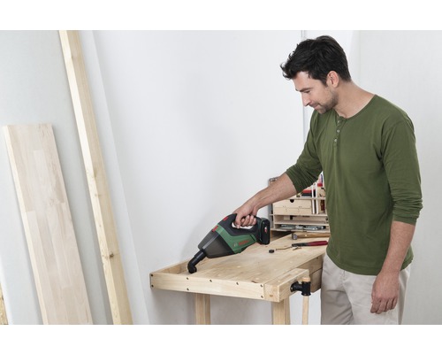 Ein Mann benutzt einen Akku Handsauger an einer Werkbank in einer Werkstatt.