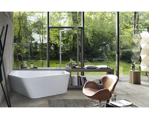 Helles Badezimmer mit Badewanne vor Fensterfront zum Garten, Sessel und Büchern