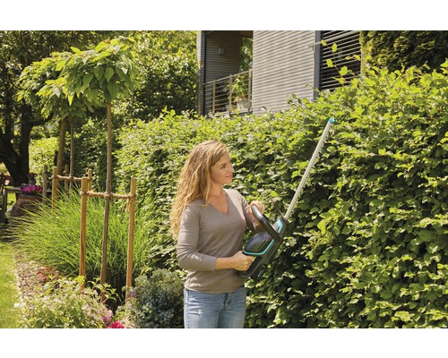 Frau schneidet Hecke mit Heckenschere im Garten.