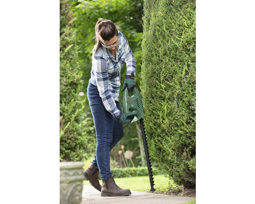 Frau schneidet Hecke mit einer Heckenschere von Bosch im Garten.