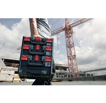 Eine Person trägt drei Metabo Werkzeugkoffer auf einer Baustelle.