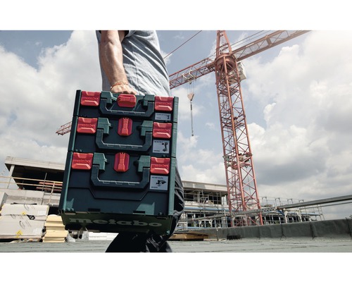 Eine Person trägt drei Metabo Werkzeugkoffer auf einer Baustelle.