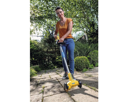 Frau benutzt einen Fugenkratzer zur Unkrautentfernung auf einem Gehweg.
