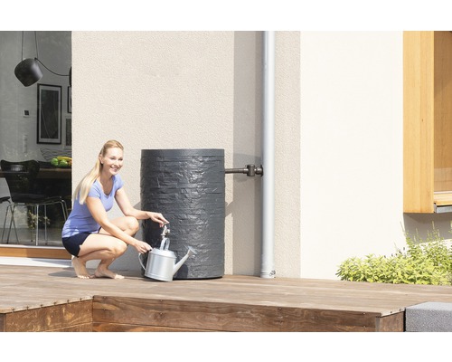 Frau befüllt Gießkanne an einer grauen Regentonne im Garten