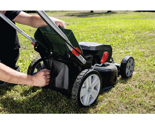 Eine Person leert den Fangkorb eines Rasenmähers auf einer Rasenfläche.