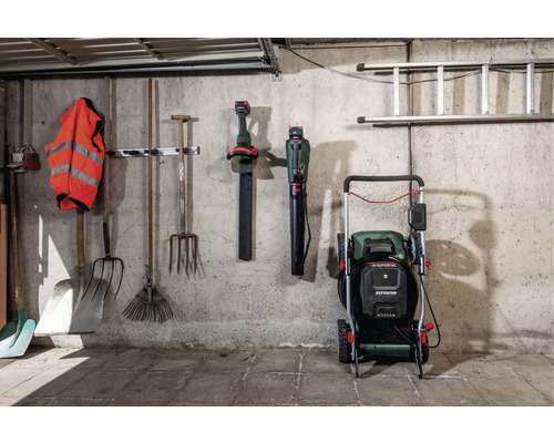 Gartenwerkzeuge, Laubbläser, Rasenmäher und Leiter an einer Wand in einer Garage.