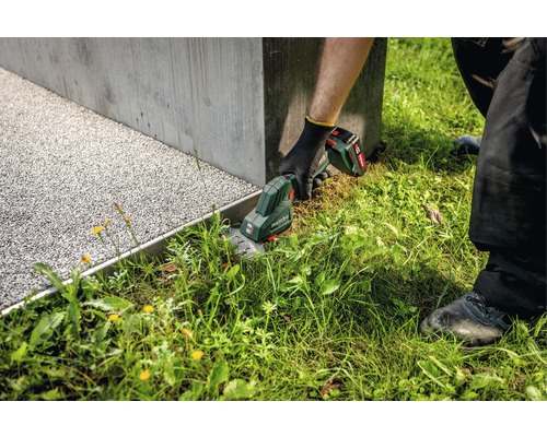 Gärtner schneidet Rasen mit einer Akku-Grasschere der Marke Metabo entlang einer Betonmauer.