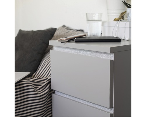 Graue Kommode mit Schubladen, auf der sich ein Handy, eine Powerbank und ein Glas Wasser befinden.